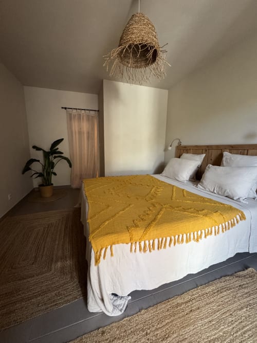 Chambre moderne au Domaine d'Olga à Aniane avec lit queen-size, plaid jaune, luminaire suspendu tressé et décoration végétale