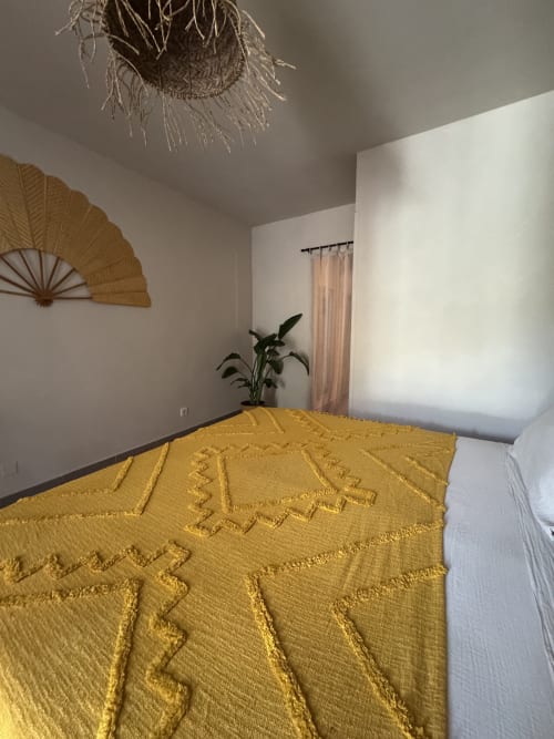 Chambre charmante au Domaine d'Olga à Aniane avec couvre-lit texturé jaune, ventilateur décoratif, plante suspendue et rideaux crème