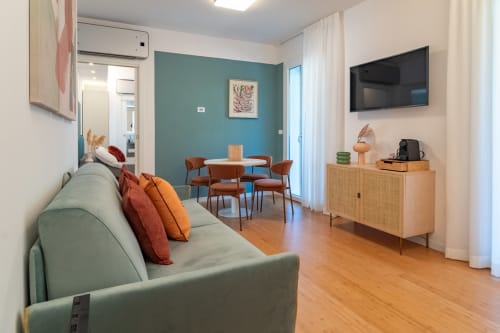Modern family suite at Pescara INN with teal accent wall, sage sofa, dining area, TV, and wooden furnishings