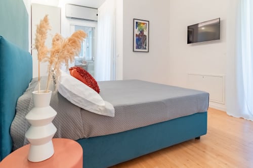 Modern bedroom at Pescara INN with teal bed base, grey mattress, pampas grass decor, and wall-mounted TV
