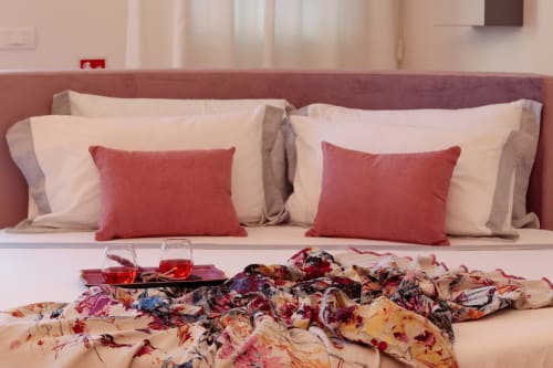 Elegant family suite at Pescara INN with burgundy headboard, cream pillows with red accents, and colorful scarves on bed