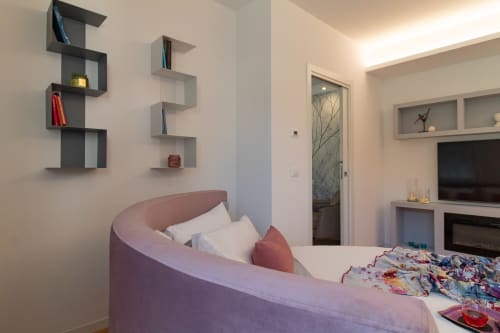 Modern bedroom at Pescara INN with curved pink chair, wall shelves, TV, and connecting suite access