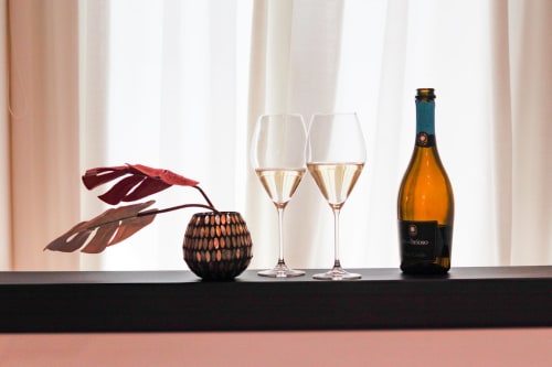 Elegant wine setup at Pescara INN with two glasses of white wine, bottle, decorative leaves, and woven sphere on black shelf