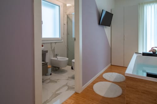 Pescara INN Family Suite bathroom entrance with lavender walls, modern sink, mounted TV, and wooden flooring with white rugs