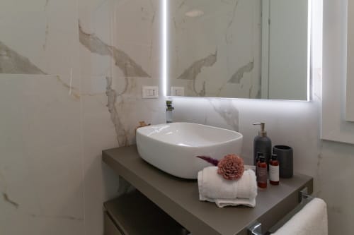 Modern bathroom in Pescara INN's Essenza Family Suite with white vessel sink, marble accent wall, and illuminated mirror