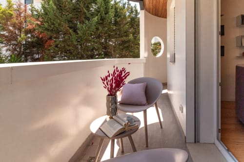 Sunny balcony at Pescara INN with gray chair, burgundy flowers, small table, and forest views