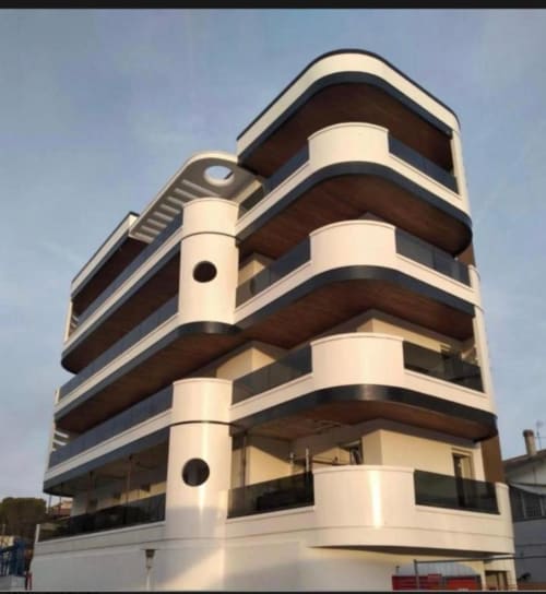 Modern curved white and brown building facade of Pescara INN hotel with balconies under blue sky