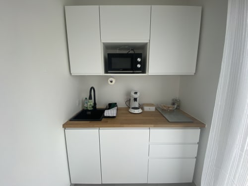 Moderne Kitchenette im Apartment La Maison Blanche mit weißen Schränken, Holzarbeitsplatte und eingebauter Mikrowelle
