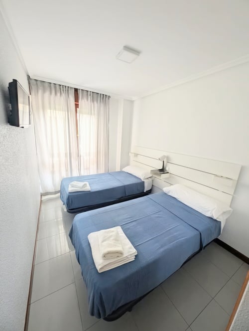 Habitación doble con dos camas azules, ropa de cama blanca, TV y baño compartido en La Ballena B&B de Santoña