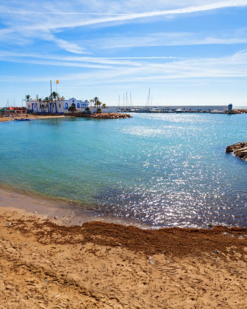Cala turquesa del Mediterráneo con playa arenosa, capilla blanca, veleros y palmeras en Hacienda Blanca, España