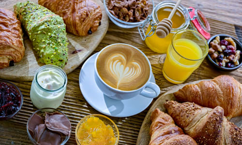 Colazione a Corte Baruzzo Relais: cappuccino, cornetti, succo d'arancia, marmellata e pasticcini freschi su tavolo in legno.