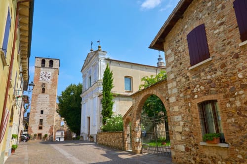 Cortile medievale in pietra della Corte Baruzzo Relais a Volta Mantovana, Italia, con torre e edifici ricoperti di edera