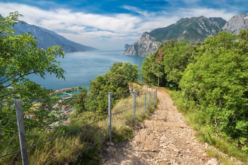 Sentiero montano con lago azzurro e scogliere drammatiche nel paesaggio lacustre italiano