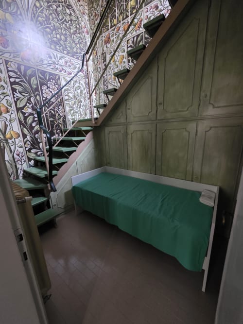 Camera da letto con letto verde, scala, carta da parati floreale ornamentale e rivestimenti color salvia nel cottage di Ravenna