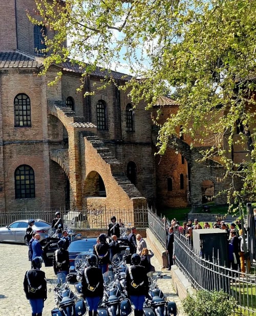 Edificio medievale in laterizio con archi a Ravenna, Italia, con moto e ospiti riuniti in cortile durante il giorno