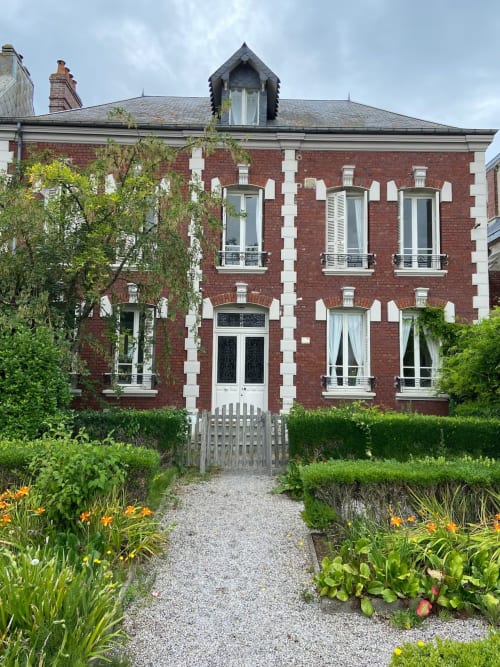 Bâtiment historique en brique rouge de l'Hôtel Hidden Bay à Cayeux-sur-Mer, aux volets blancs et jardins aménagés