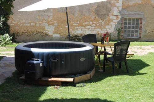 Bain à remous gonflable noir dans le jardin du Madiana 89 B&B à Bellechaume, avec espace de détente et bâtisse en pierre rustique