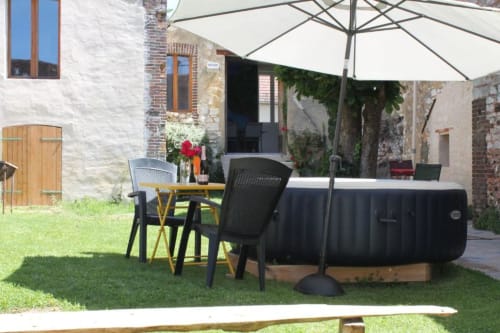 Terrasse de jardin extérieure du gîte Madiana 89 B&B avec bain à remous noir, table de repas, parasol et bâtisse en pierre rustique à Bellechaume.