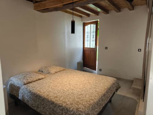 Chambre Coco à la Maison d'hôtes Madiana 89 à Bellechaume avec lit à parure patterned, poutres apparentes et porte d'entrée sur jardin
