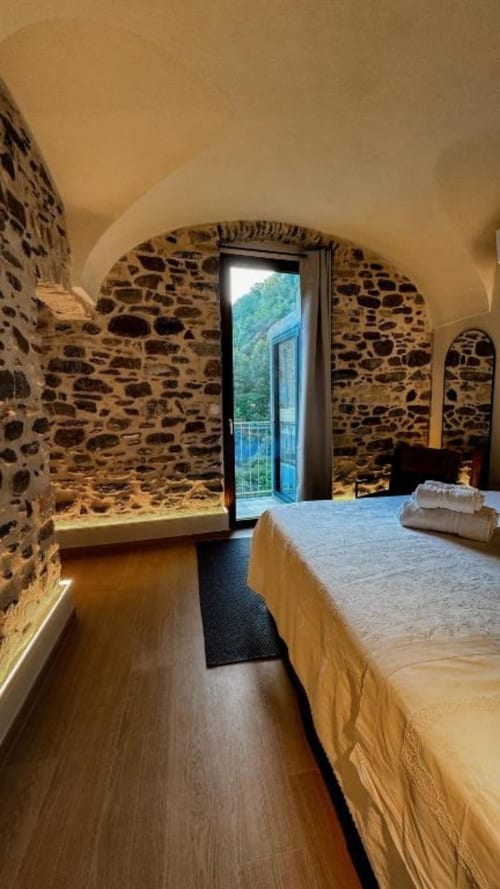 Arched stone bedroom with bed, wooden floors, and balcony view in Dolceacqua B&B