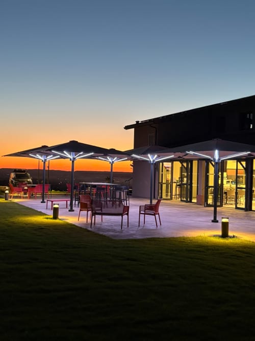 Terrasse du Lieu-dit Boulage au coucher de soleil avec parasols, mobilier et bâtiment moderne illuminé à Marquefave