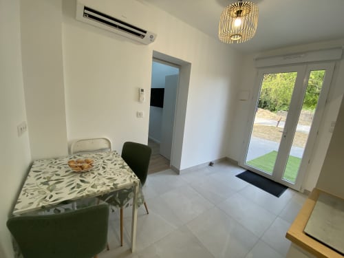 Modern apartment interior at La Maison Blanche with dining table, kitchen, glass doors opening to garden, and air