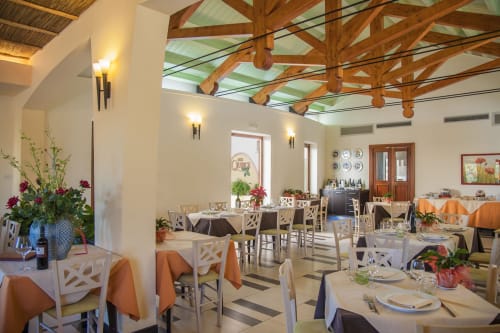 Elegante sala da pranzo dell'Hotel Ristorante alle Querce a Castelbuono con travi in legno, sedie bianche e centrotavola floreali.