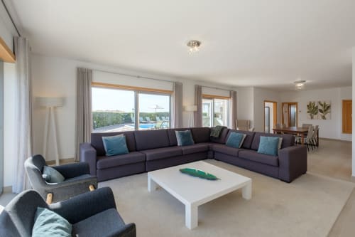 Sala de estar de villa moderna no Be SilverCoast com sofá seccional roxo, vistas da piscina e do mar através das grandes janelas, Serra D'El