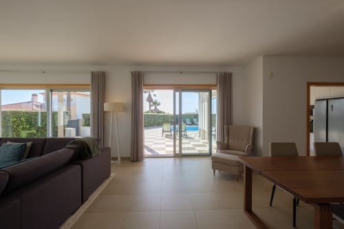 Sala de estar de villa moderna com vista para piscina, mesa de jantar, sofá escuro e portas de vidro que se abrem para o terraço em Be SilverCoast, Serra