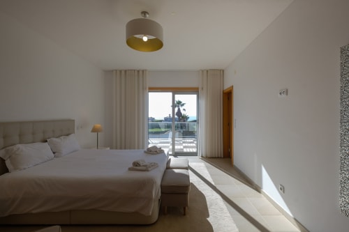 Quarto moderno na villa Be SilverCoast com vista para a piscina, cama, portas de vidro para o terraço e palmeiras
