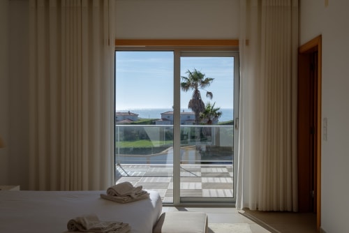 Interior luminoso da villa Be SilverCoast com portas de vidro abrindo para piscina e vistas de palmeiras em Serra D'El Rei, Portugal