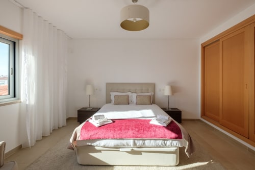 Quarto luminoso na Villa Maravilhosa do Be SilverCoast, Serra D'El Rei, com cama, manta rosa, guarda-roupa de madeira e vista para a piscina