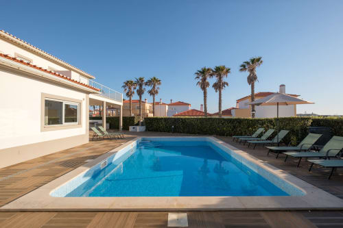 Villa Magnífica SilverCoast com piscina, espreguiçadeiras, palmeiras e edifícios estilo mediterrânico em Serra d'El Rei, Portugal
