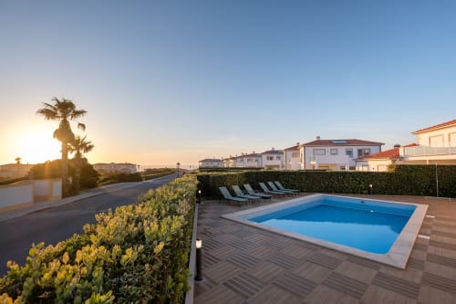 Piscina da villa SilverCoast ao pôr do sol com espreguiçadeiras, palmeiras e casarões costeiros em Serra D'El Rei, Portugal