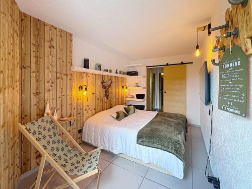Chambre douillette ski-in aux murs en pin, lit double, fauteuil et décor de chalet de montagne aux Tanières de Montgenèvre