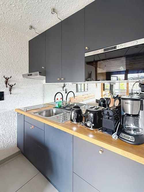 Cuisine moderne de l'appartement Les Tanières avec armoires sombres, plan de travail en bois, électroménagers inox et rangements intégrés