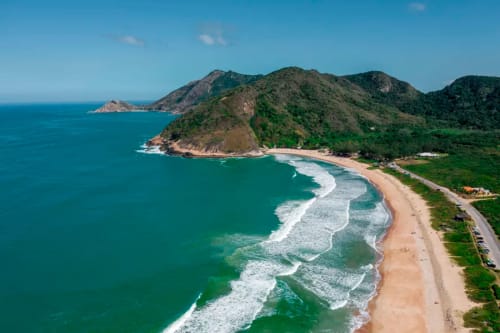 Praia costeira com montanhas verdejantes, ondas oceânicas turquesas e litoral arenoso perto do Rio de Janeiro