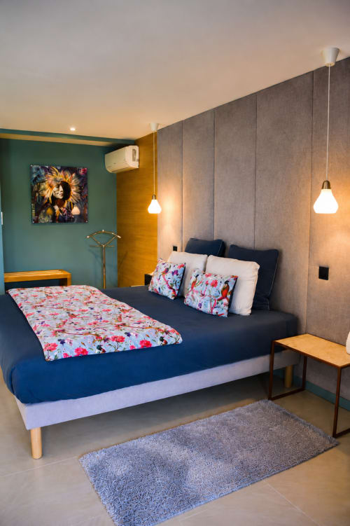 Chambre moderne à l'hôtel Au Pied Des Oliviers à Calenzana avec lit bleu marine, coussins fleuris, mur d'accent gris et suspension