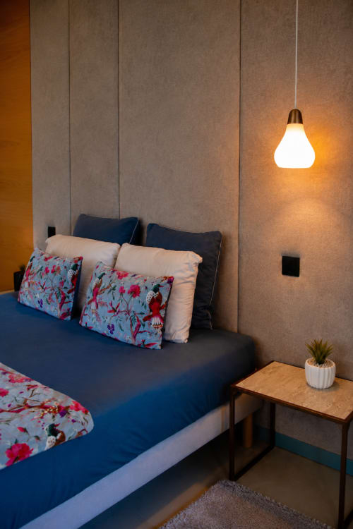 Chambre moderne à l'Au Pied Des Oliviers avec lit bleu, oreillers fleuris, luminaire suspendu et table de nuit en bois à Calenzana