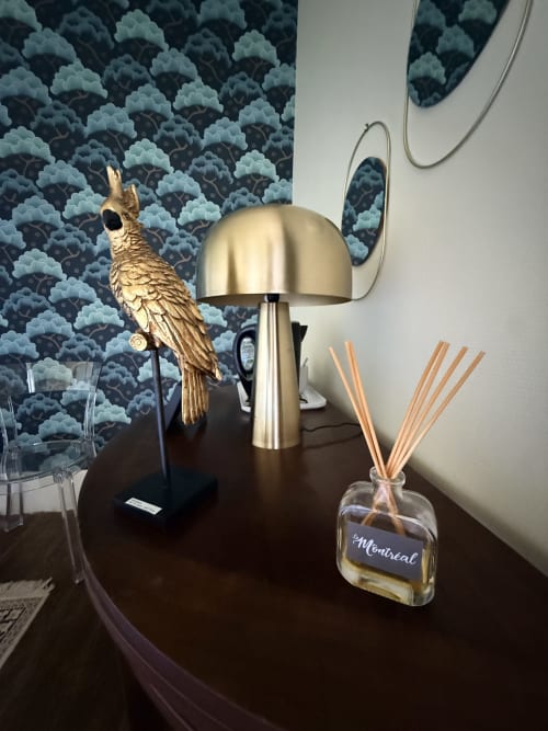 Décor de la suite Montreal Tokyo : statuette de perroquet doré, lampe en laiton, diffuseur de roseaux Montreal sur table foncée