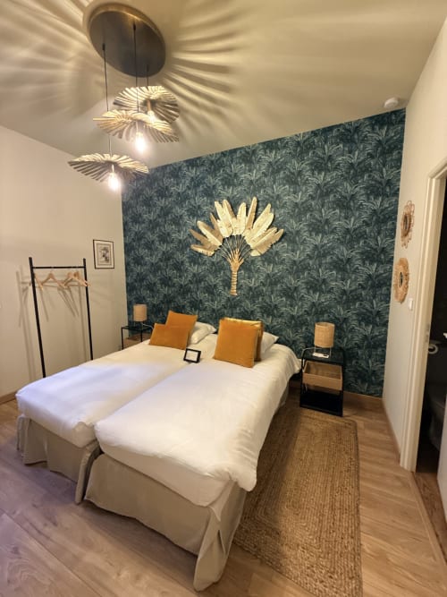 Chambre moderne au Le Montreal avec lits blancs, mur d'accent à motifs turquoise, décor palmier doré et luminaires suspendus à Montréal