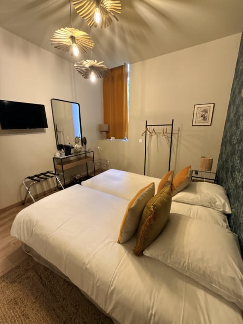 Chambre moderne au Le Montreal BnB à Montréal du Gers avec lits jumeaux, luminaires suspendus dorés, TV et mobilier contemporain.