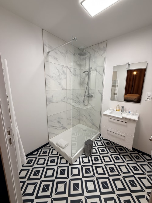Salle de bain moderne du gîte Le Montreal B&B à Montréal du Gers avec douche à l'italienne en marbre, vasque blanche et carrelage géométrique noir