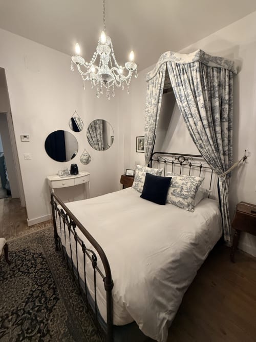 Chambre élégante au gîte Le Montreal à Montréal du Gers avec lit à baldaquin, lustre en cristal et rideaux à motif toile de Jouy