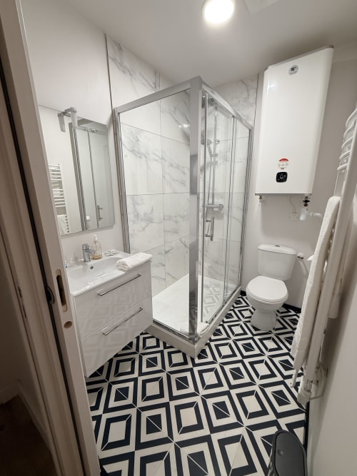 Salle de bain moderne au Le Montreal B&B à Montréal du Gers avec douche en marbre, vasque blanche et carrelage géométrique