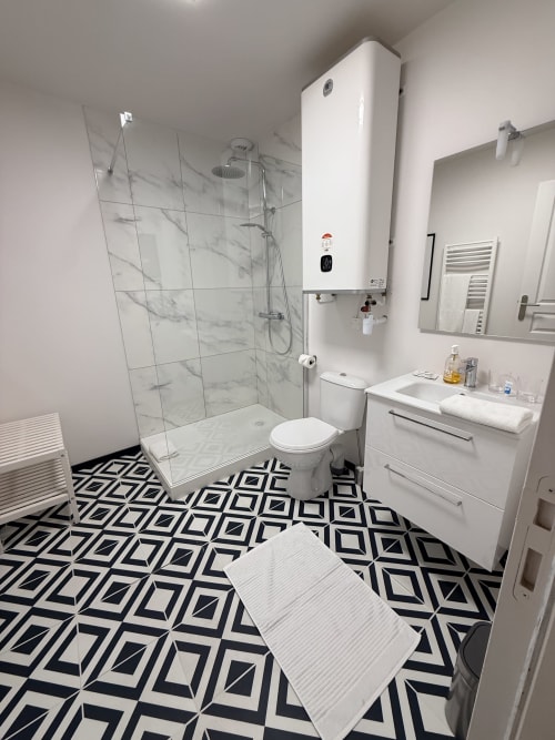 Salle de bains moderne au gîte Le Montreal à Montréal du Gers : douche ouverte, vasque blanche et carrelage géométrique noir et blanc