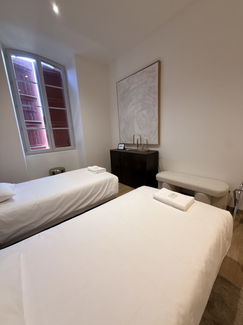 Deux lits jumeaux dans la chambre moderne du B&B Le Montreal à Montréal du Gers, avec vue sur la ville et art mural abstrait