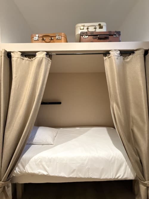 Lit de style vintage aux rideaux beige et literie blanche au Le Montreal BnB à Montréal du Gers
