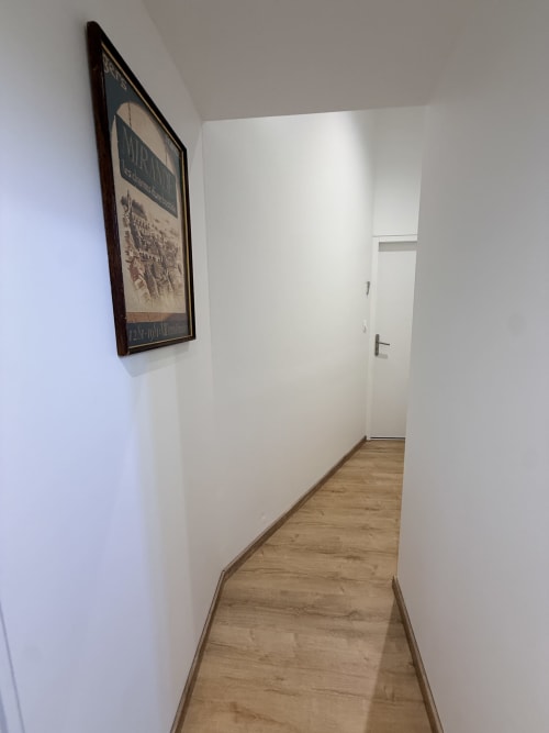 Couloir étroit au B&B Le Montreal à Montréal du Gers avec plancher en bois et murs blancs, affiche encadrée à gauche, porte au