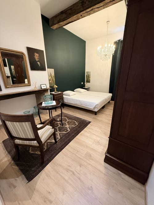 Chambre élégante au Le Montreal B&B à Montréal du Gers avec mur d'accent vert, lit blanc, lustre et mobilier d'époque